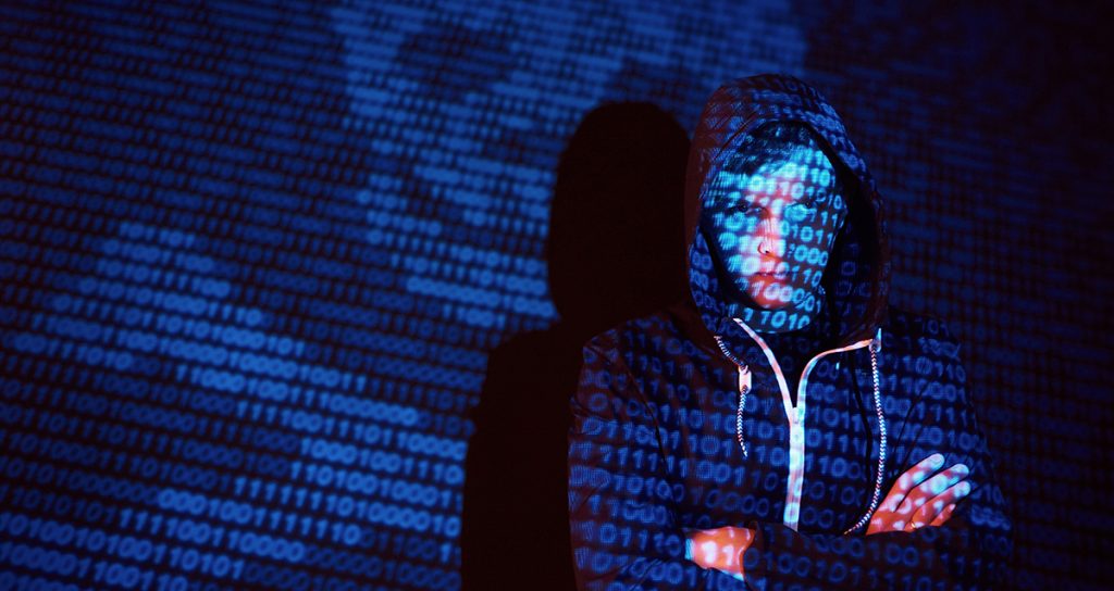 A hooded hacker with his face obscured by website code